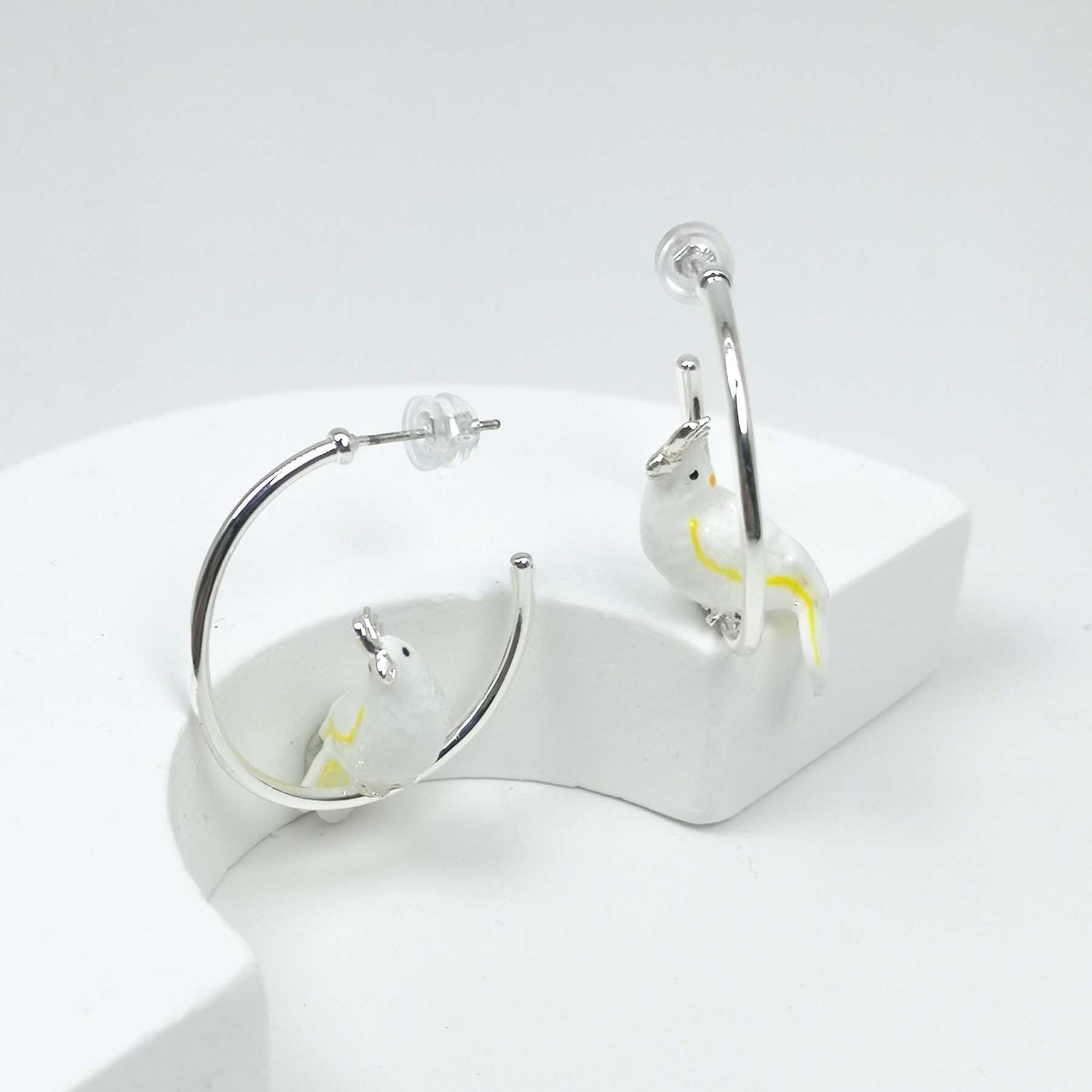 Silver hoop earrings with yellow accents on a white stand