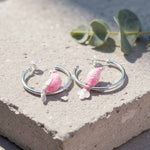 Silver hoop earrings with pink and white bird charms on a concrete surface.