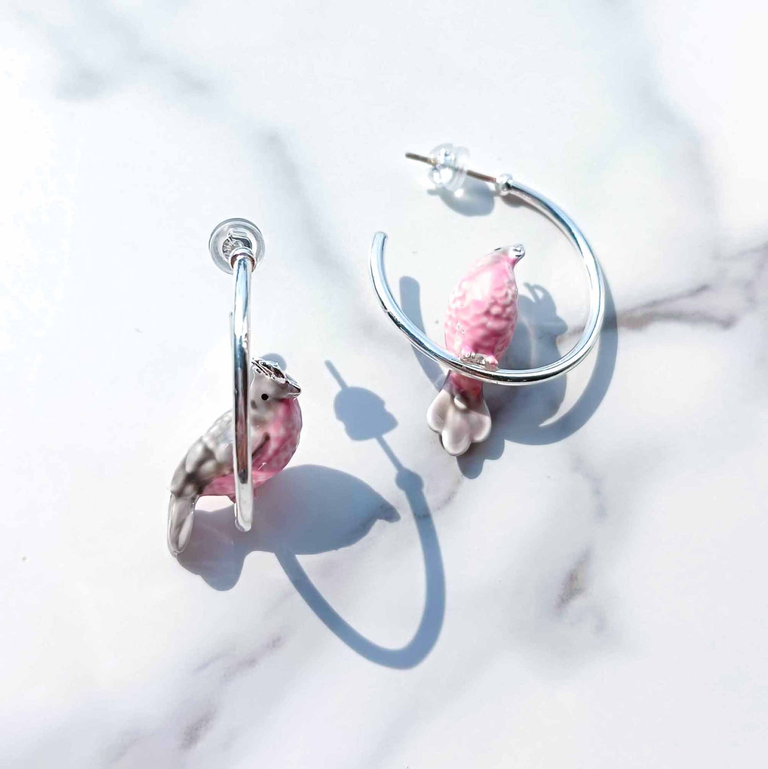 Pair of hoop earrings with pink and gray charms on a light background