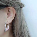 Earring with a pink cockatoo and silver design worn by a person with long hair.