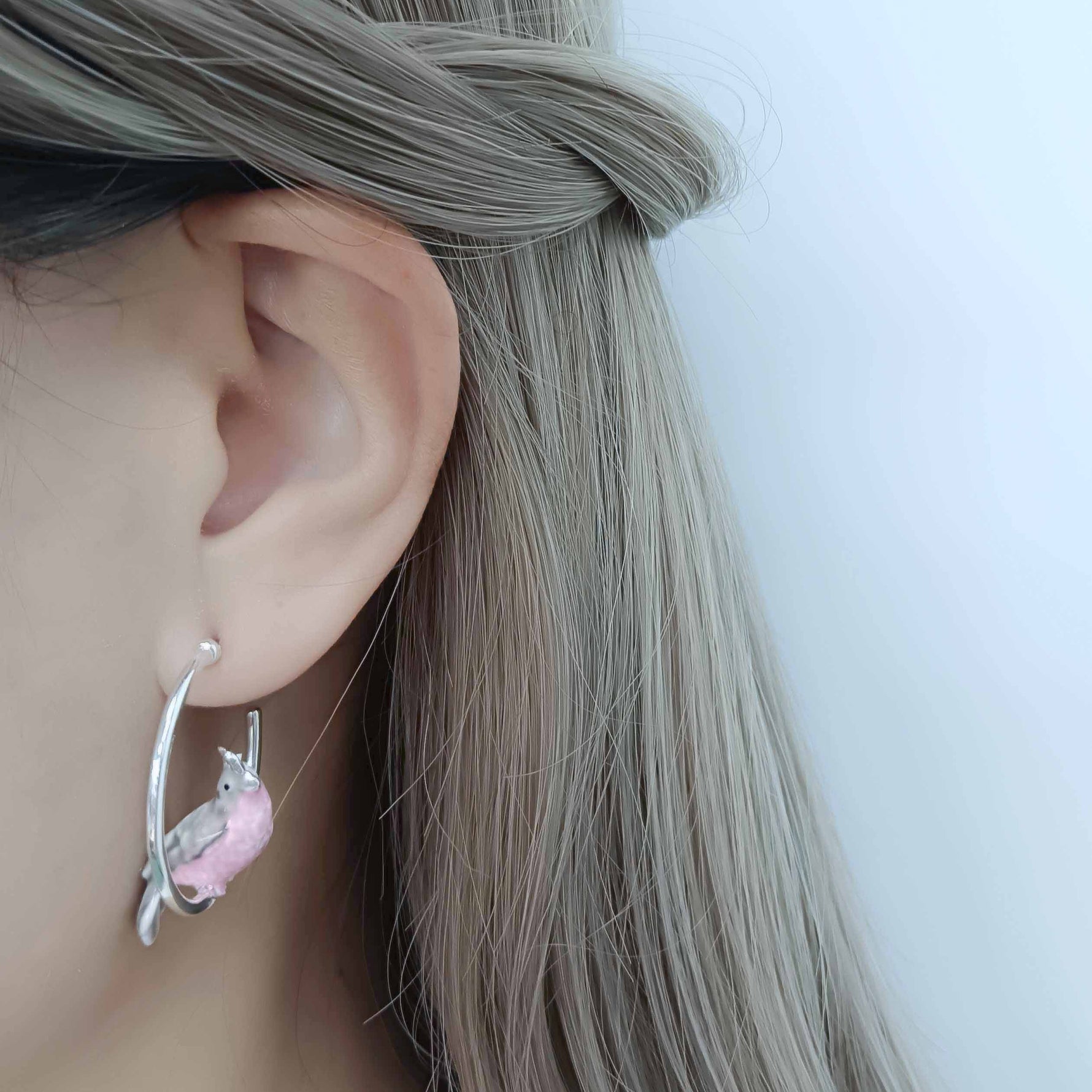 Earring with a pink cockatoo and silver design worn by a person with long hair.