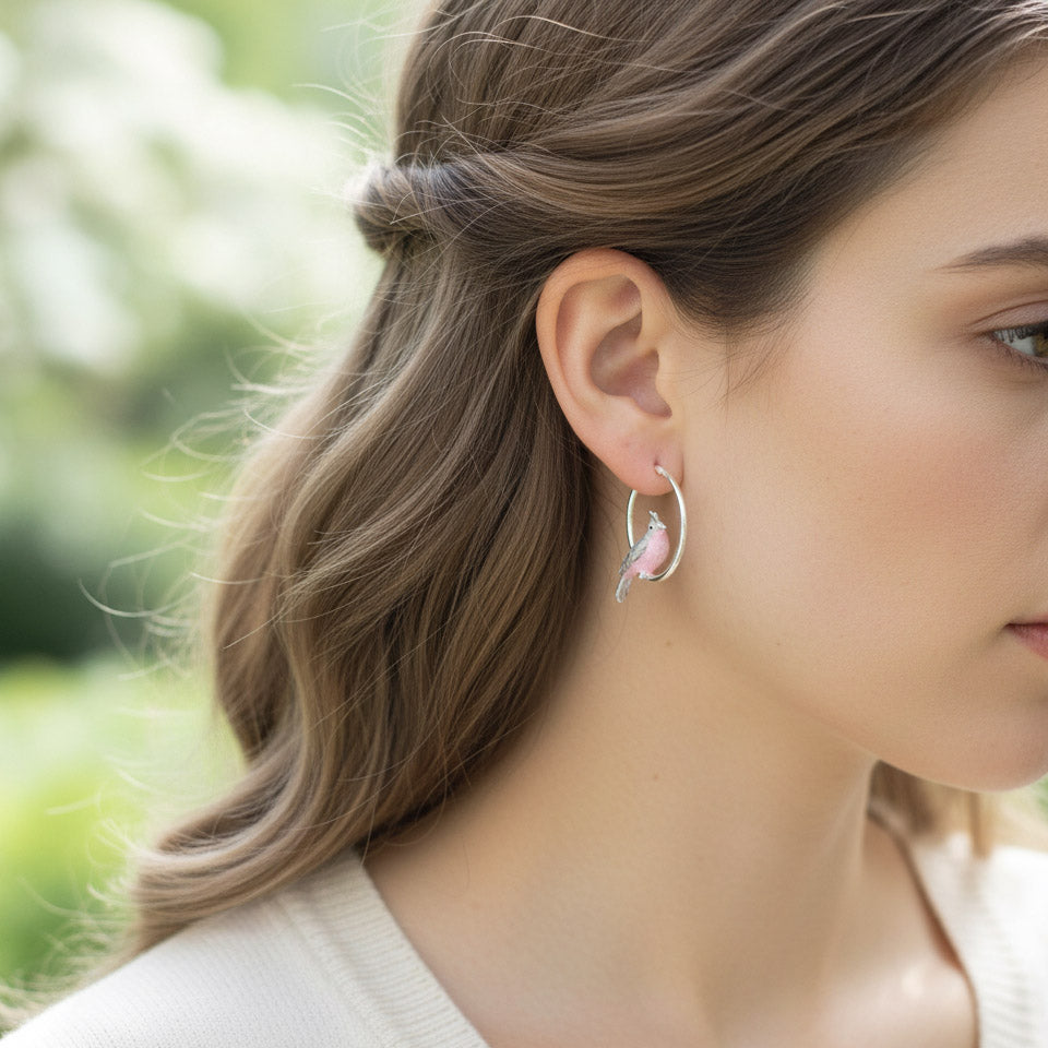 Model wearing silver hoop earrings with pink enamel bird design, handcrafted cockatoo earrings inspired by nature.