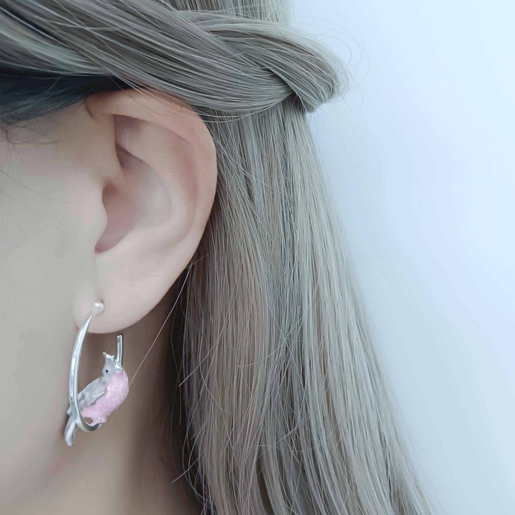 Earring with a small animal design worn by a person with gray hair.