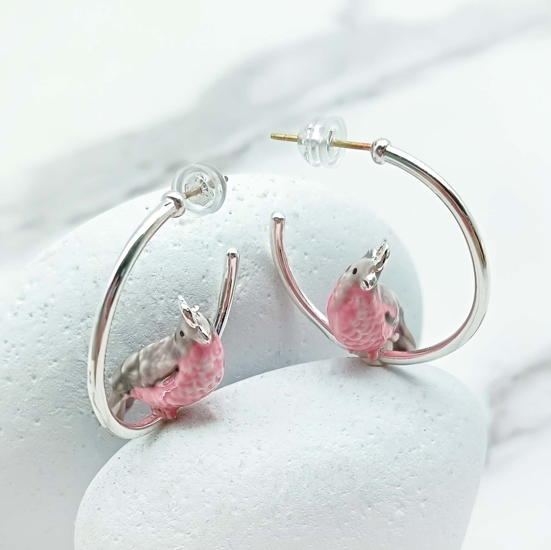Silver hoop earrings with pink and gray bird designs on a white background
