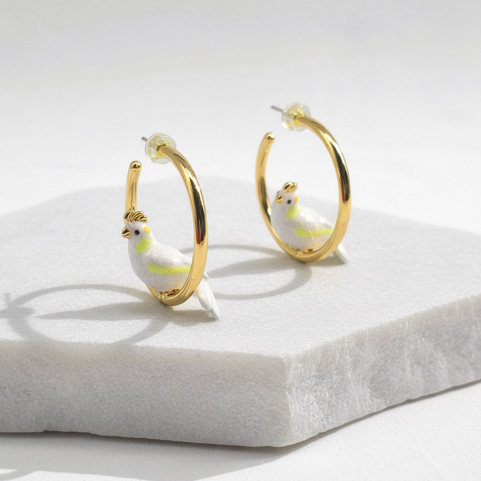 Gold hoop earrings with bird charms on a white surface