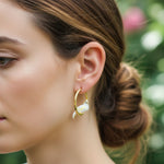 Close-up of a woman wearing gold hoop earrings with a blurred natural background