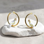 Gold hoop earrings with cockatoo designs on a white stone surface