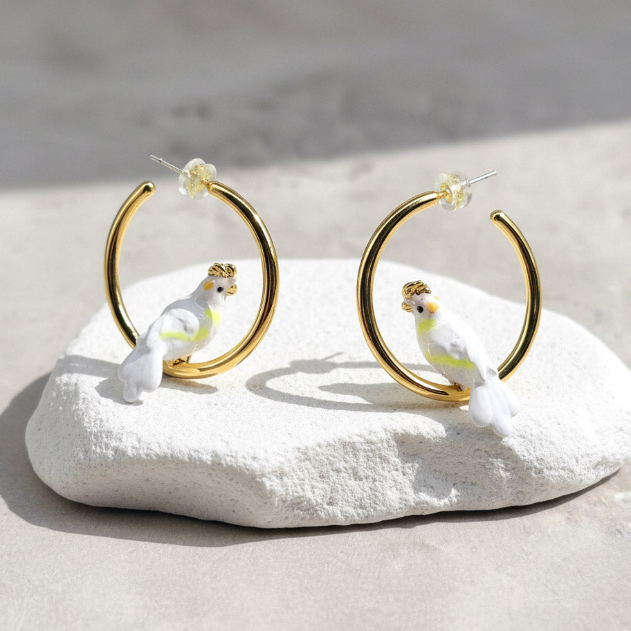 Gold hoop earrings with cockatoo designs on a white stone surface