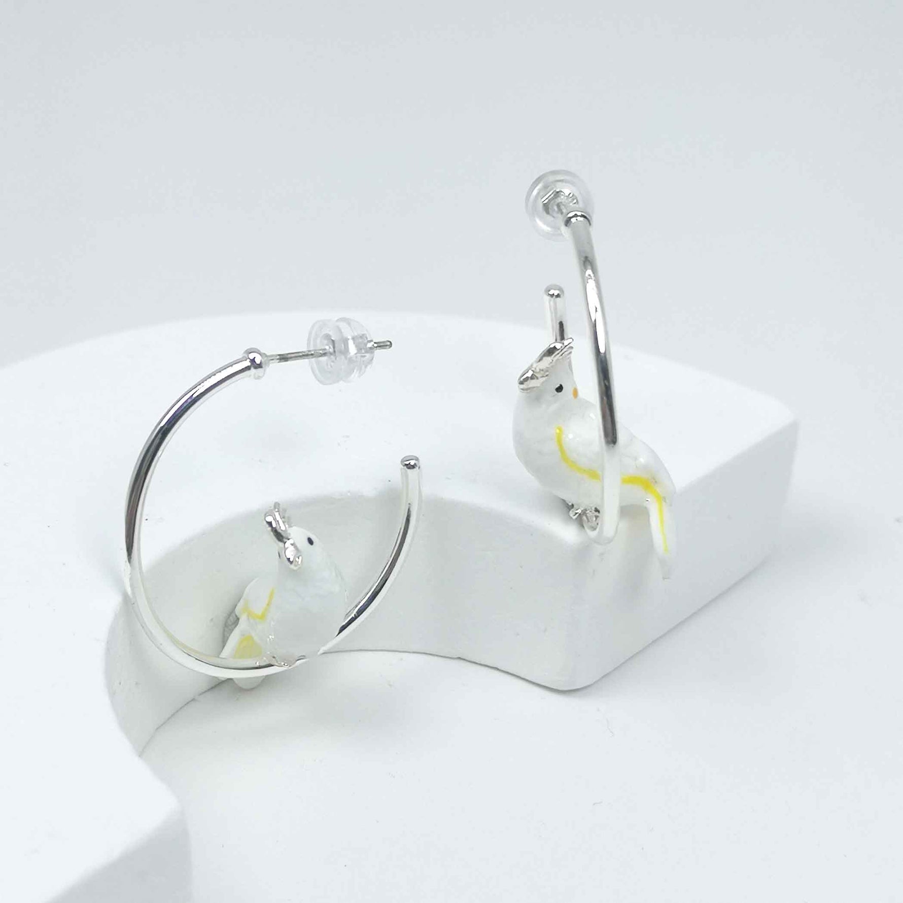 Silver-plated hoop earrings with white enamel cockatoo bird accents, a whimsical and chic statement for everyday wear