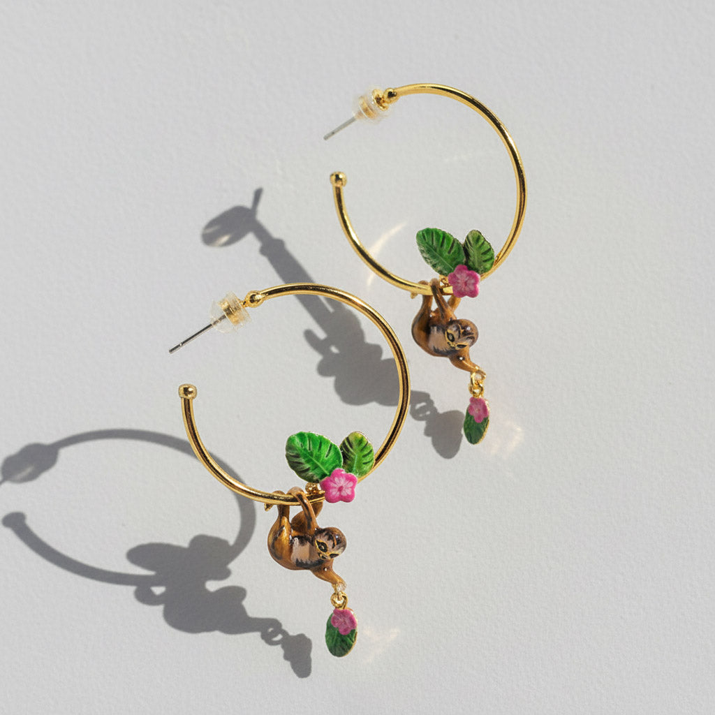 Gold hoop earrings with green leaves  pink flowers and a sloth on a light gray background