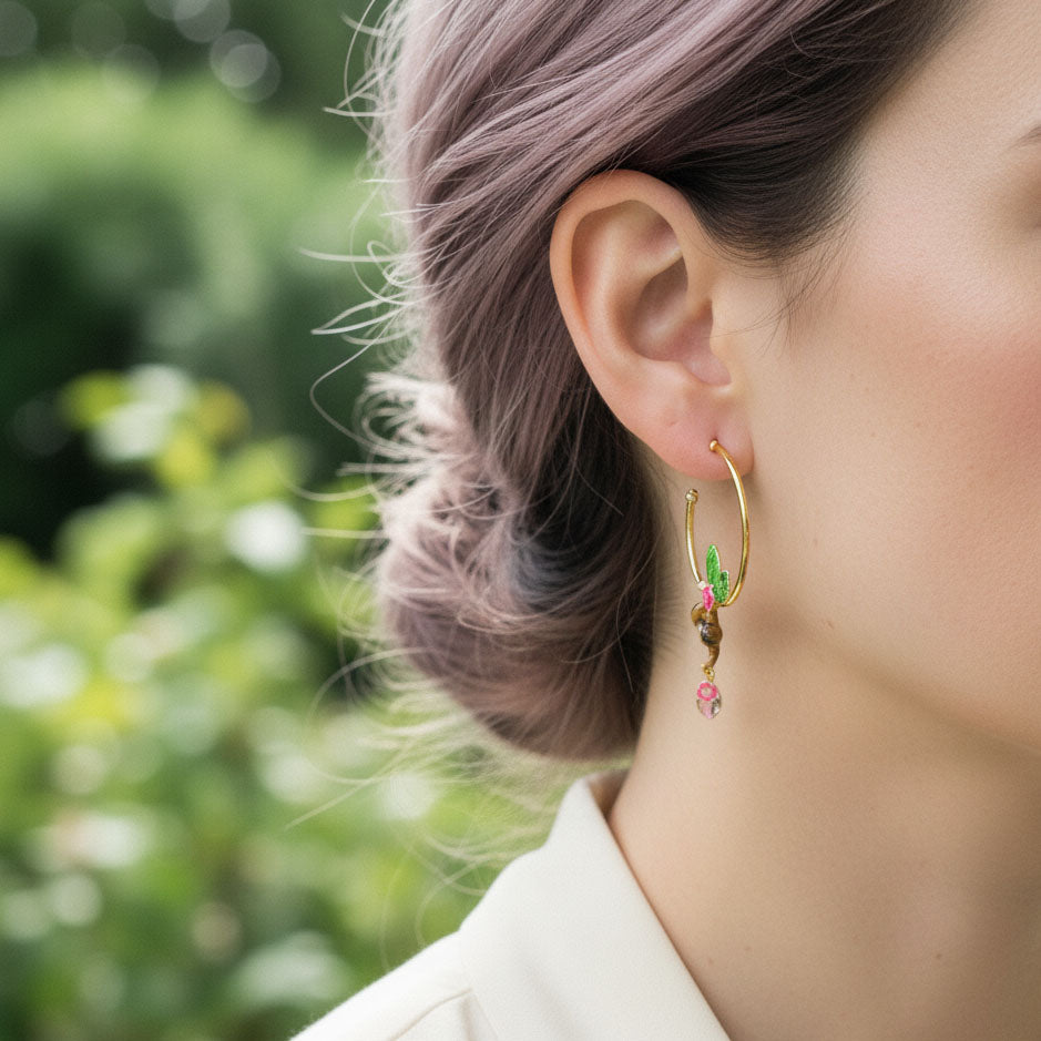 Close-up of a person wearing gold hoop earrings with floral designs against a blurred green background