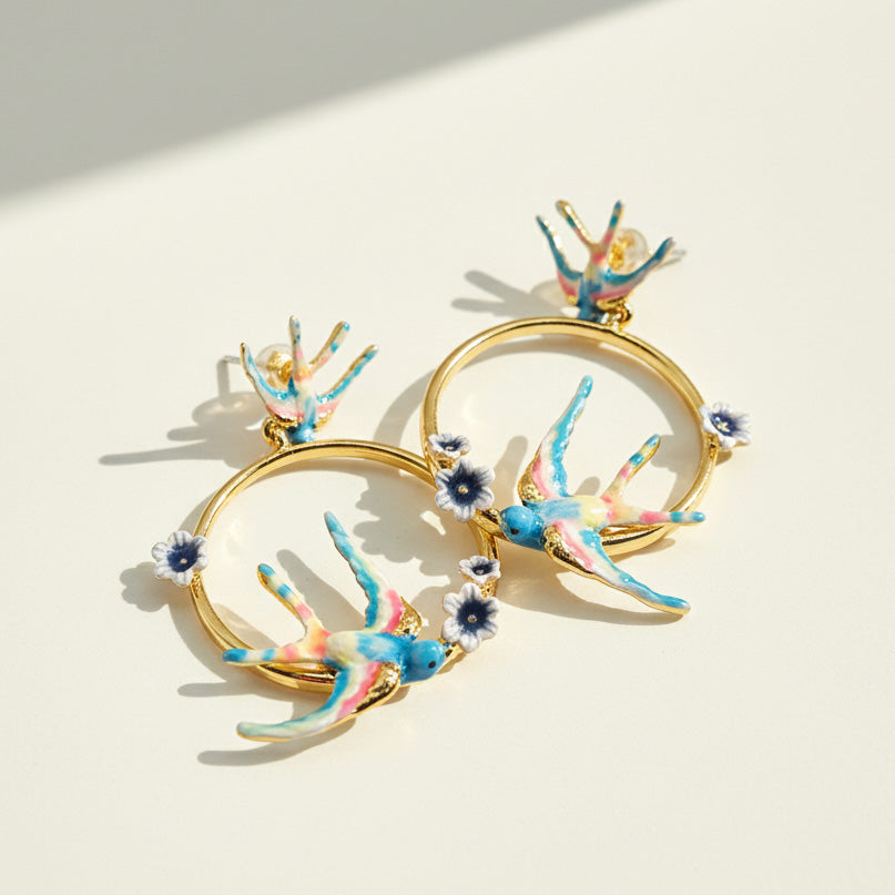 Gold hoop earrings with colorful bird designs on a light background