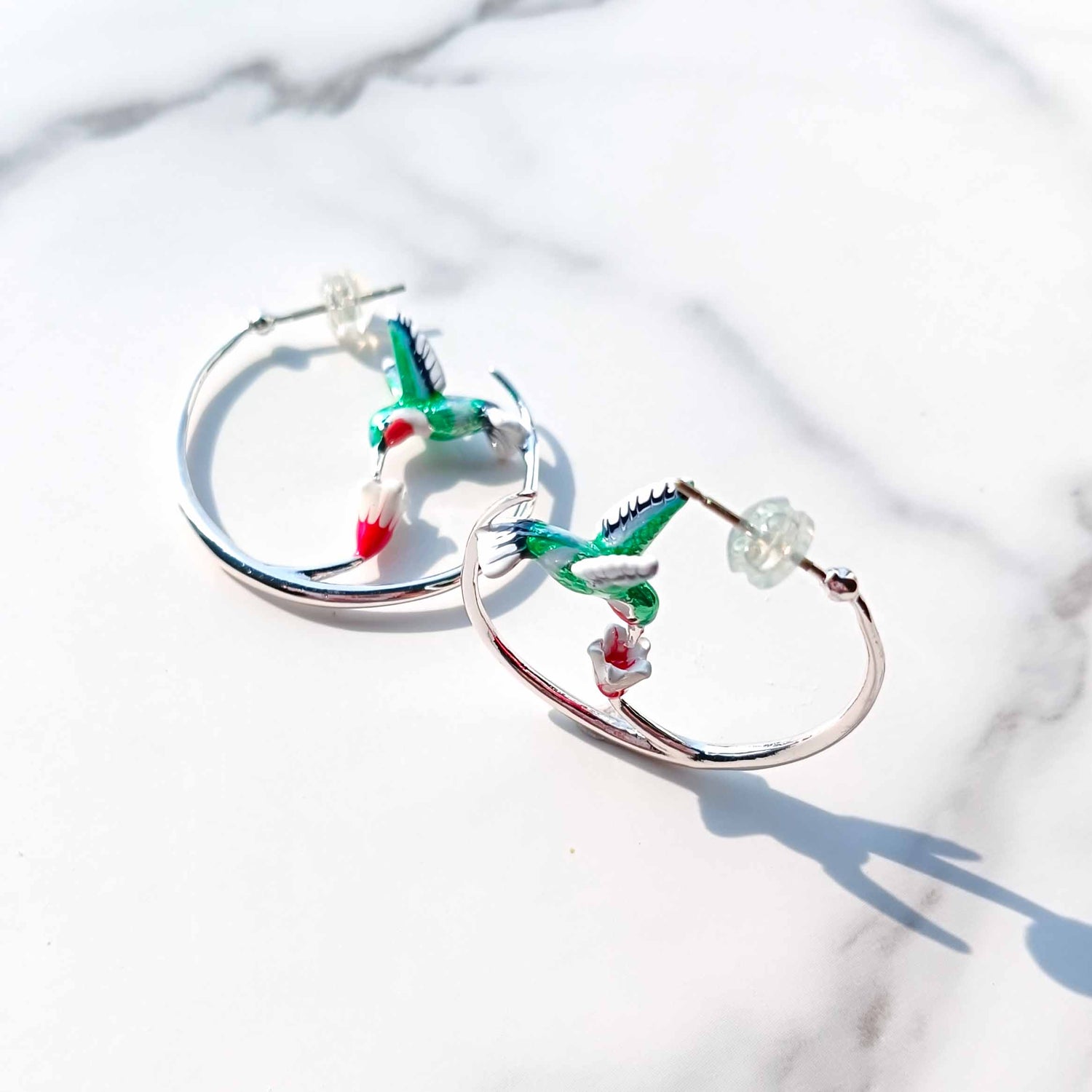 Hoop earrings with hummingbird designs on a white marble background