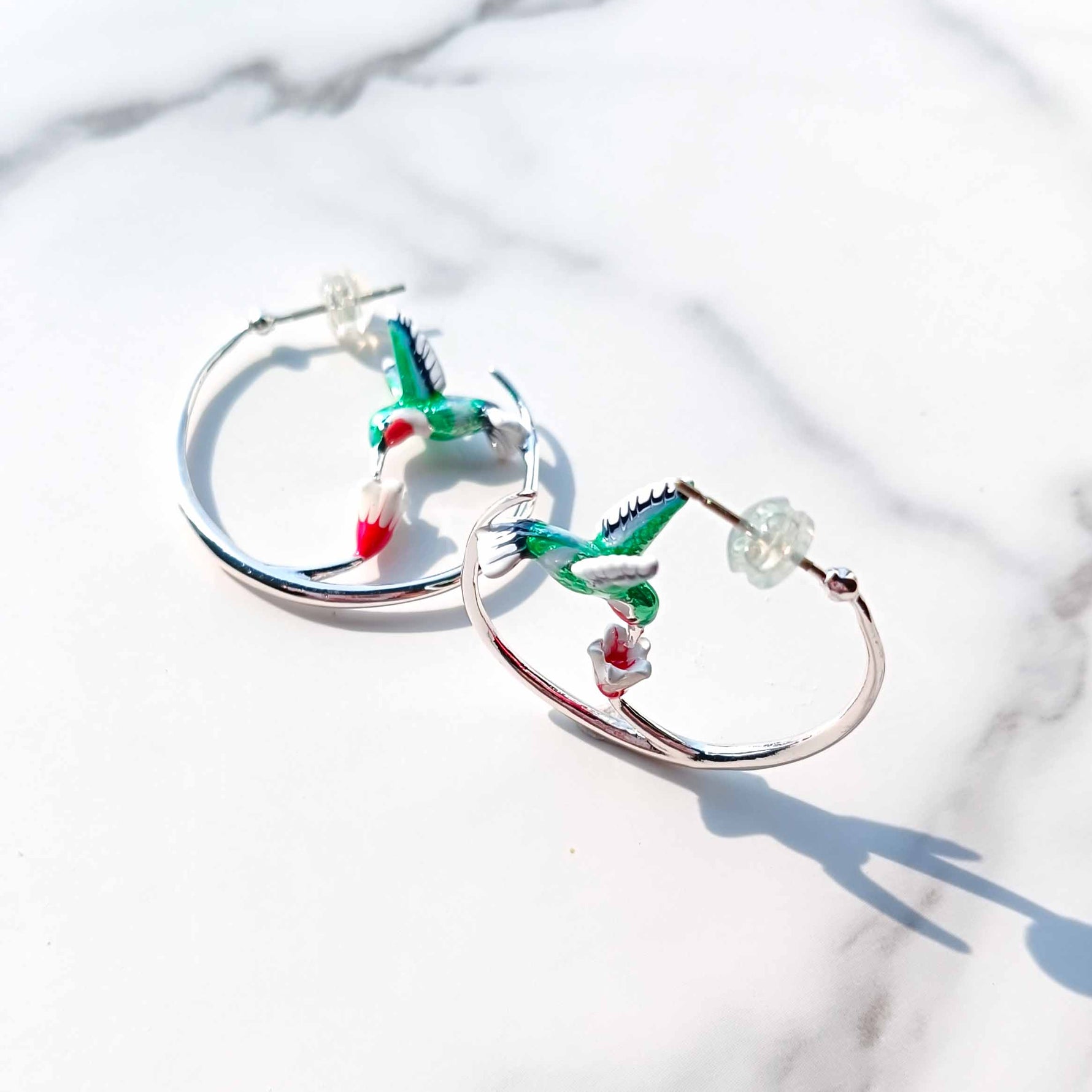 Hoop earrings with hummingbird designs on a white marble background