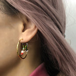 Close-up of an ear with a gold hoop earring featuring hummingbird.