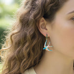 Close-up of a woman wearing colorful bird-shaped earrings with blurred greenery in the background
