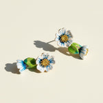 Floral earrings with blue, white, and green colors on a beige background