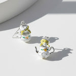 Teapot and mouse earrings on a light surface with soft shadows