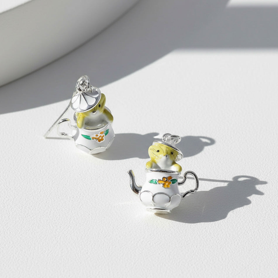 Teapot and mouse earrings on a light surface with soft shadows
