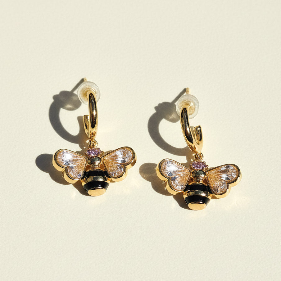 Gold bee-shaped earrings with gemstones on a beige background