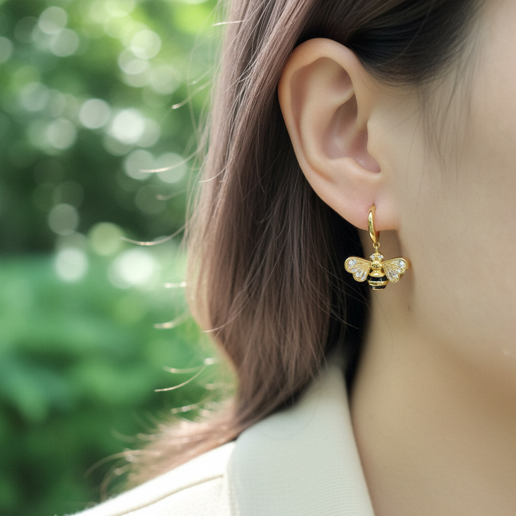Gold bee-shaped earring worn by a person with a blurred green background