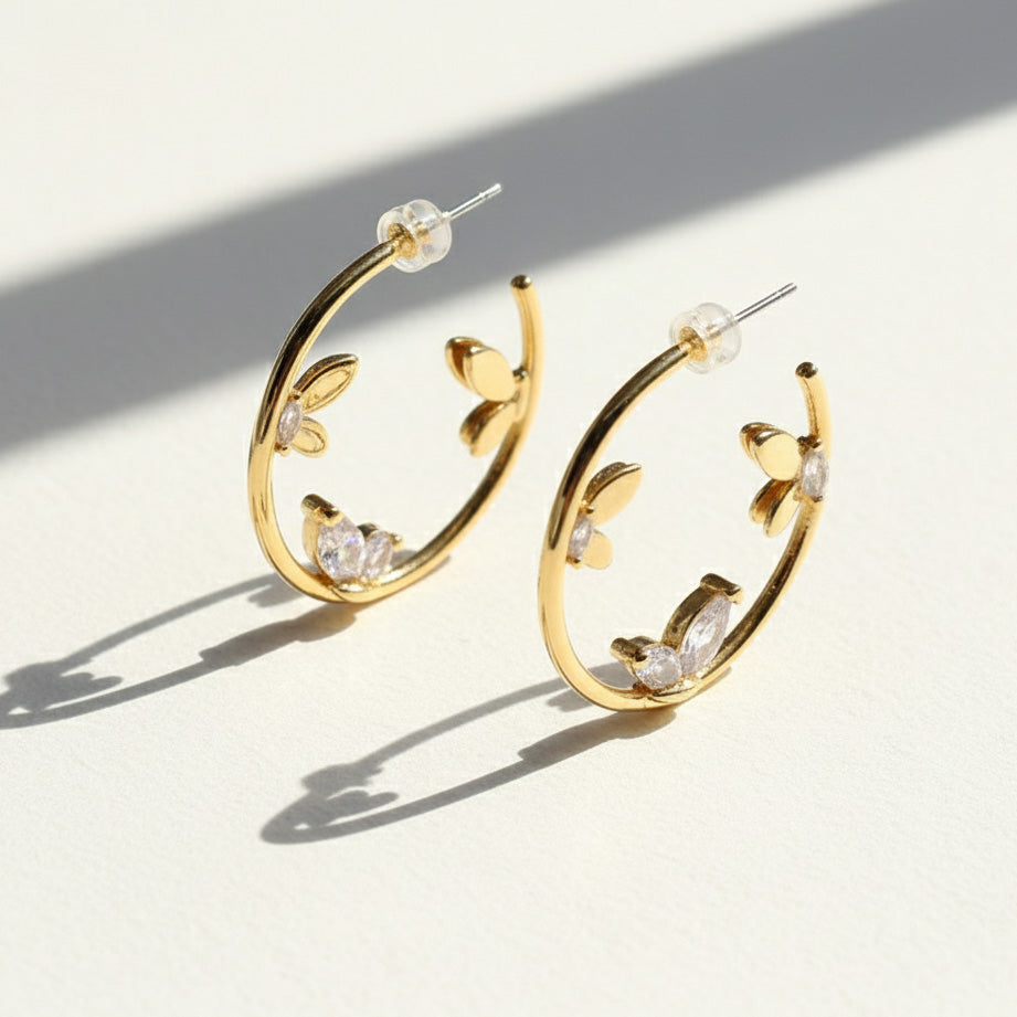 Gold hoop earrings with leaf and crystal details on a light background
