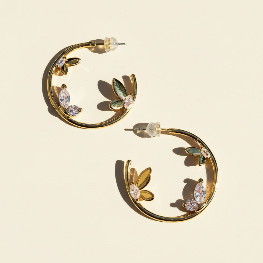 Gold hoop earrings with leaf and gemstone details on a beige background