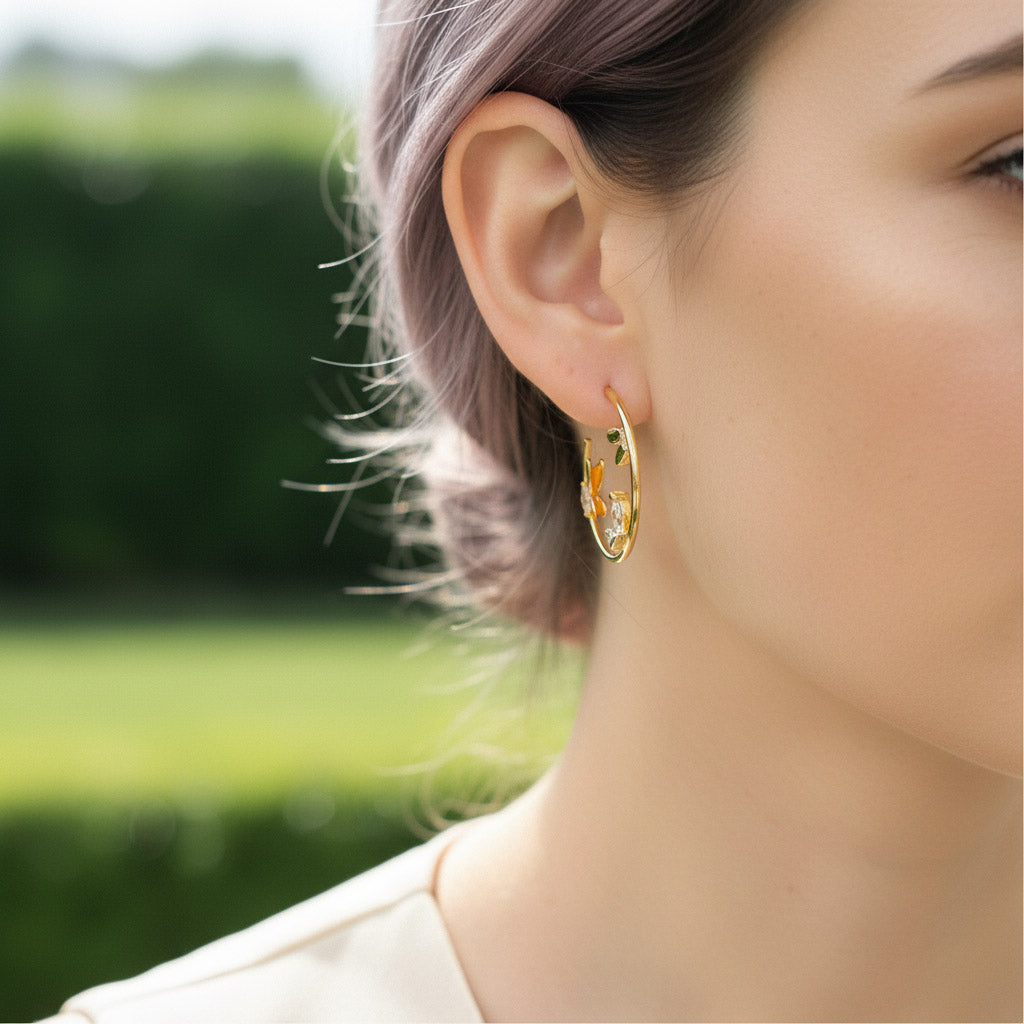 Close-up of a person wearing gold hoop earrings with a blurred green outdoor background