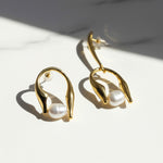 Gold earrings with pearl drops on a light surface