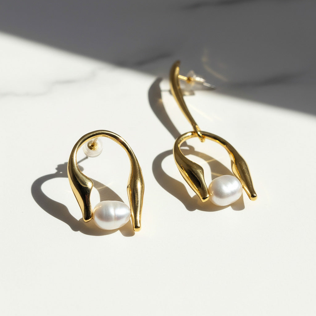 Gold earrings with pearl drops on a light surface