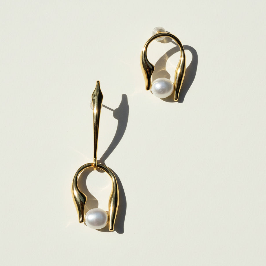 Gold earrings with pearls on a light background