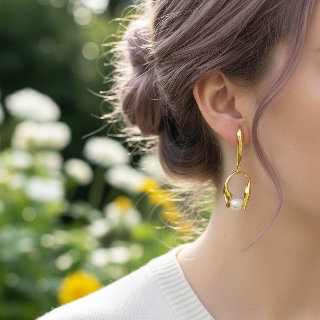 Gold hoop earrings with a pearl accent worn by a person with blurred floral background
