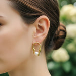 Gold hoop earring with a pearl on a blurred natural background