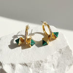 Gold and green earrings on a textured white surface
