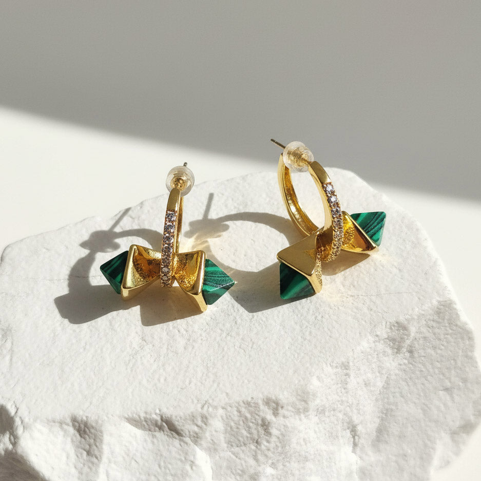 Gold and green earrings on a textured white surface