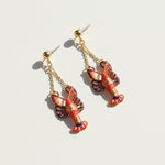 Lobster-shaped earrings with gold chains on a light background