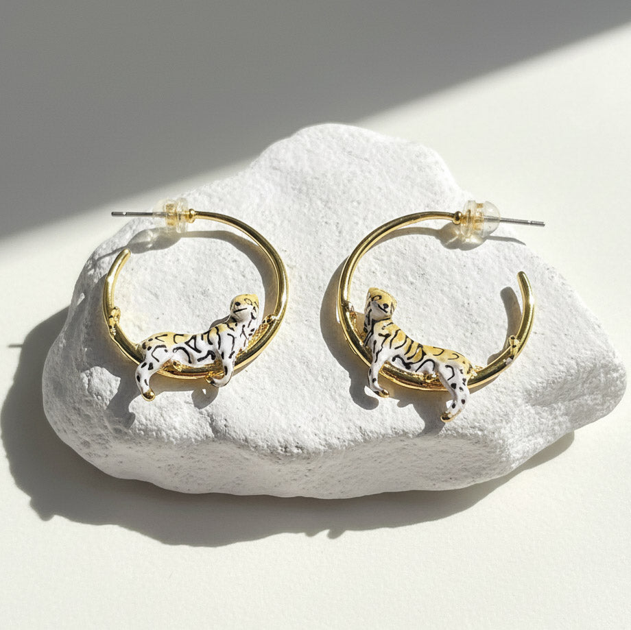 Gold hoop earrings with tiger designs on a white stone surface