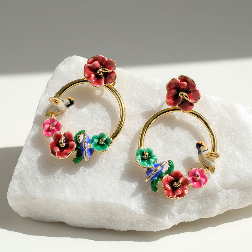 Pair of gold hoop earrings with colorful floral designs on a white stone surface.