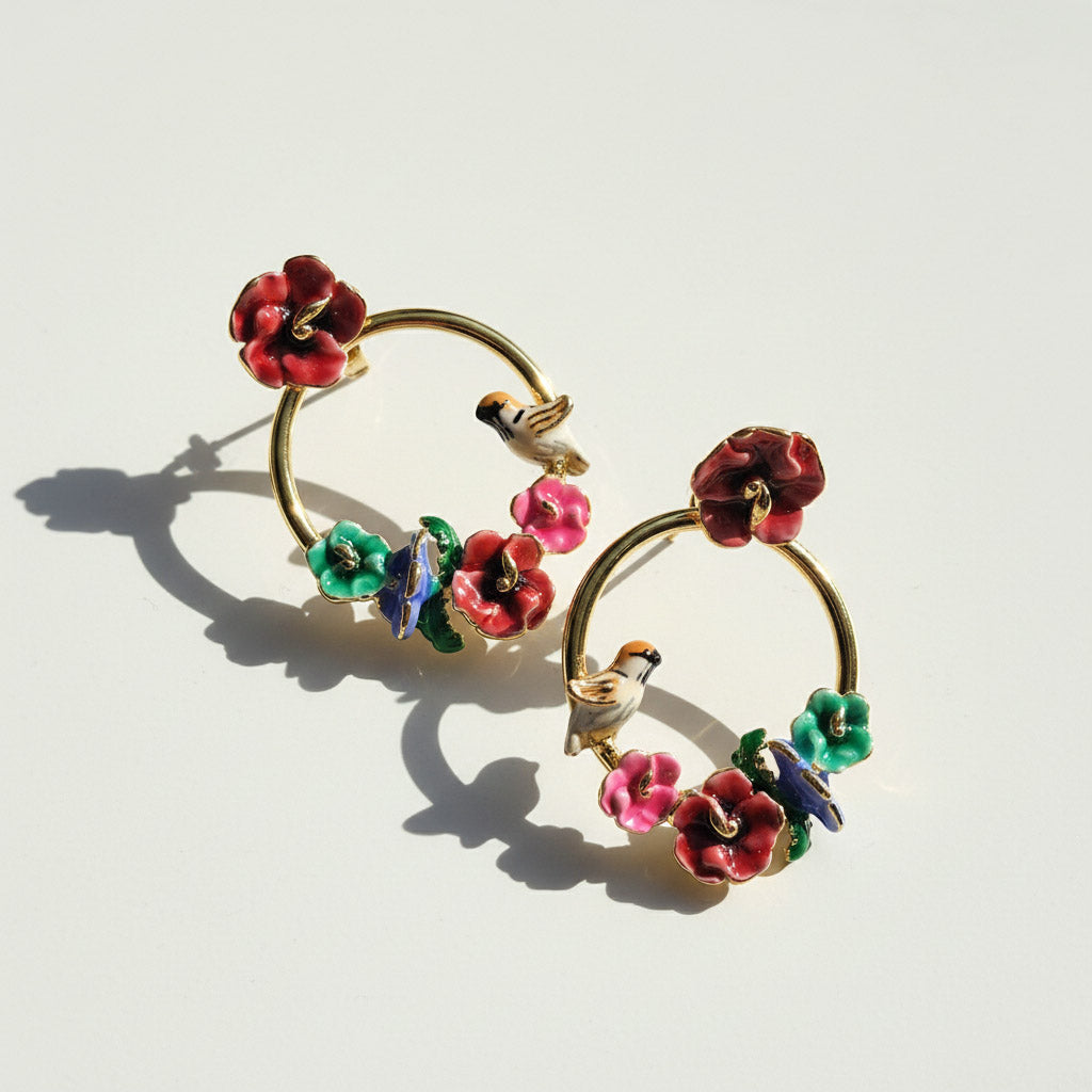 Gold hoop earrings with colorful floral and bird designs on a light background