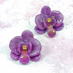 Purple flower-shaped earrings with gold centers on a light pink background