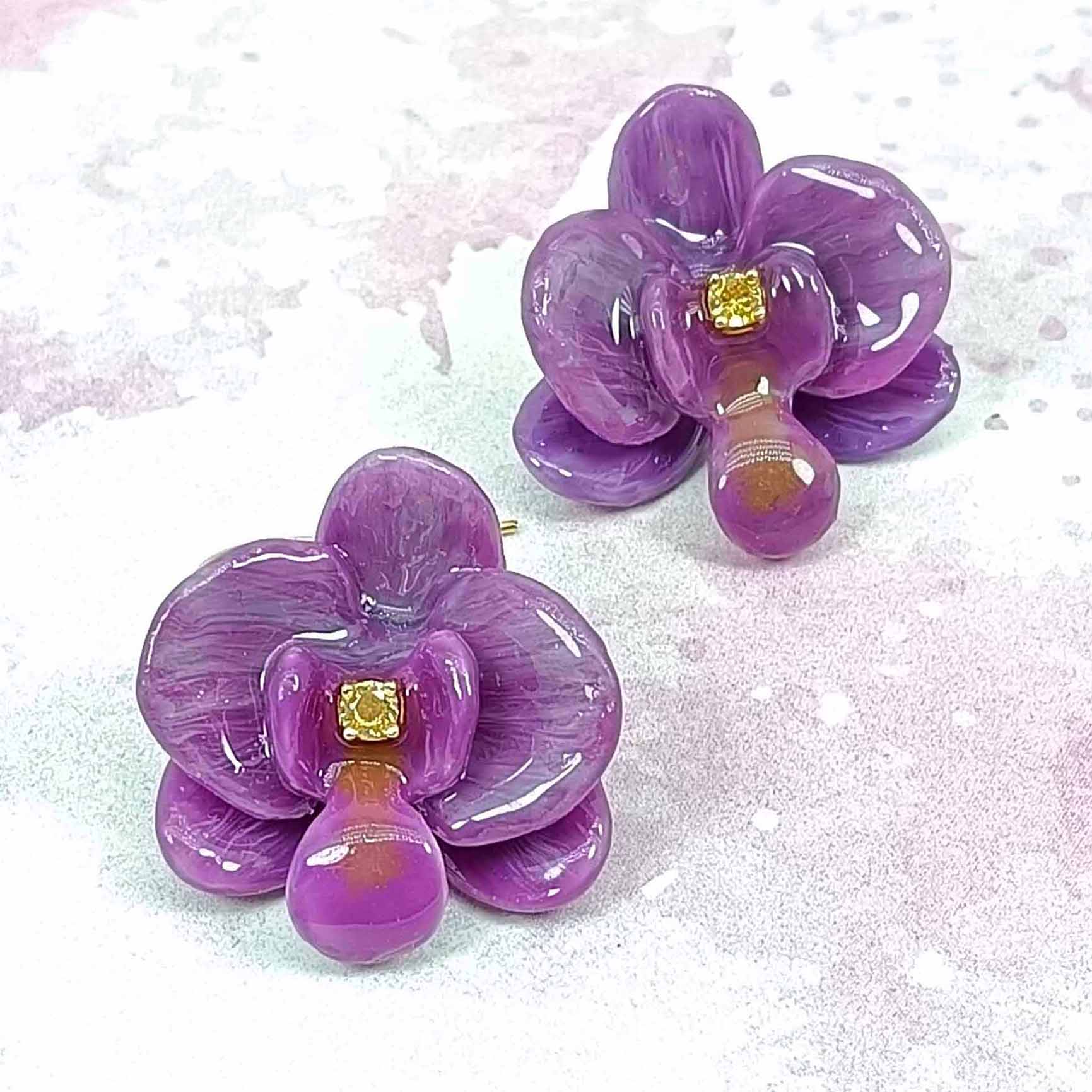 Purple flower-shaped earrings with gold centers on a light pink background