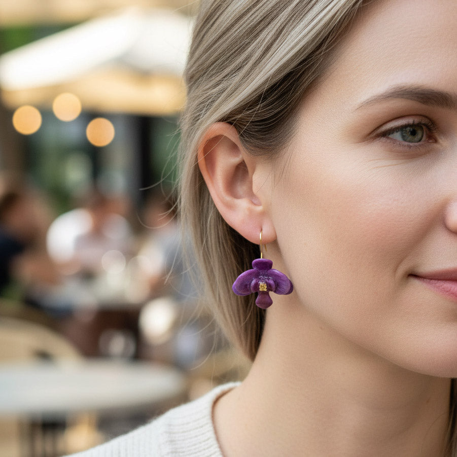 Model wearing a handcrafted purple orchid flower earring with gold hook, photographed outdoors in natural light