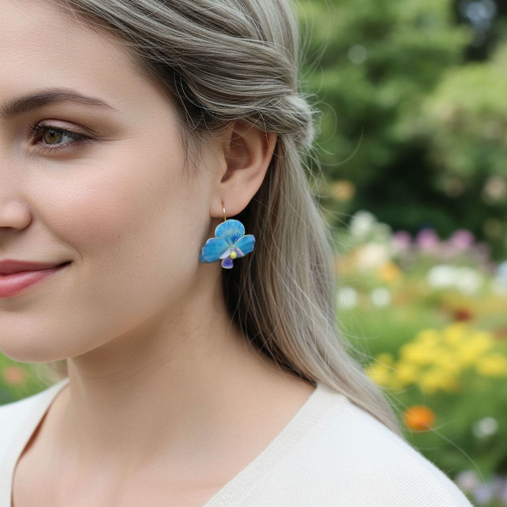 Woman wearing blue flower earrings with a blurred garden background