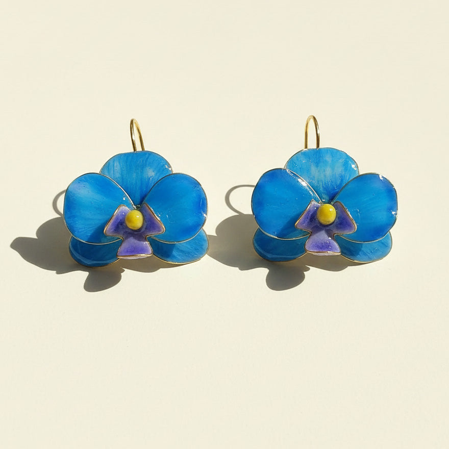Pair of blue flower-shaped earrings on a beige background
