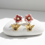Flower-shaped earrings with bee details on a white stone surface