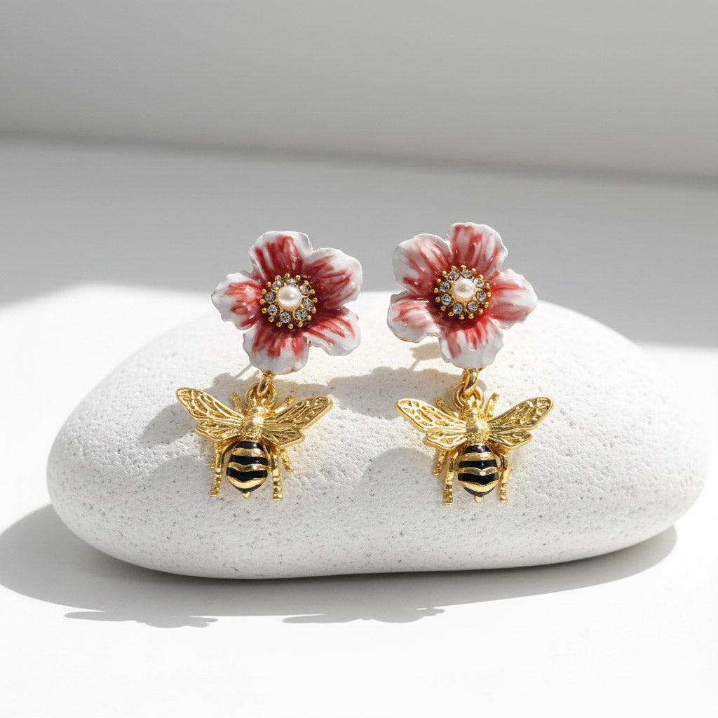 Flower-shaped earrings with bee details on a white stone surface