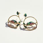 Gold hoop earrings with colorful gemstones on a light background