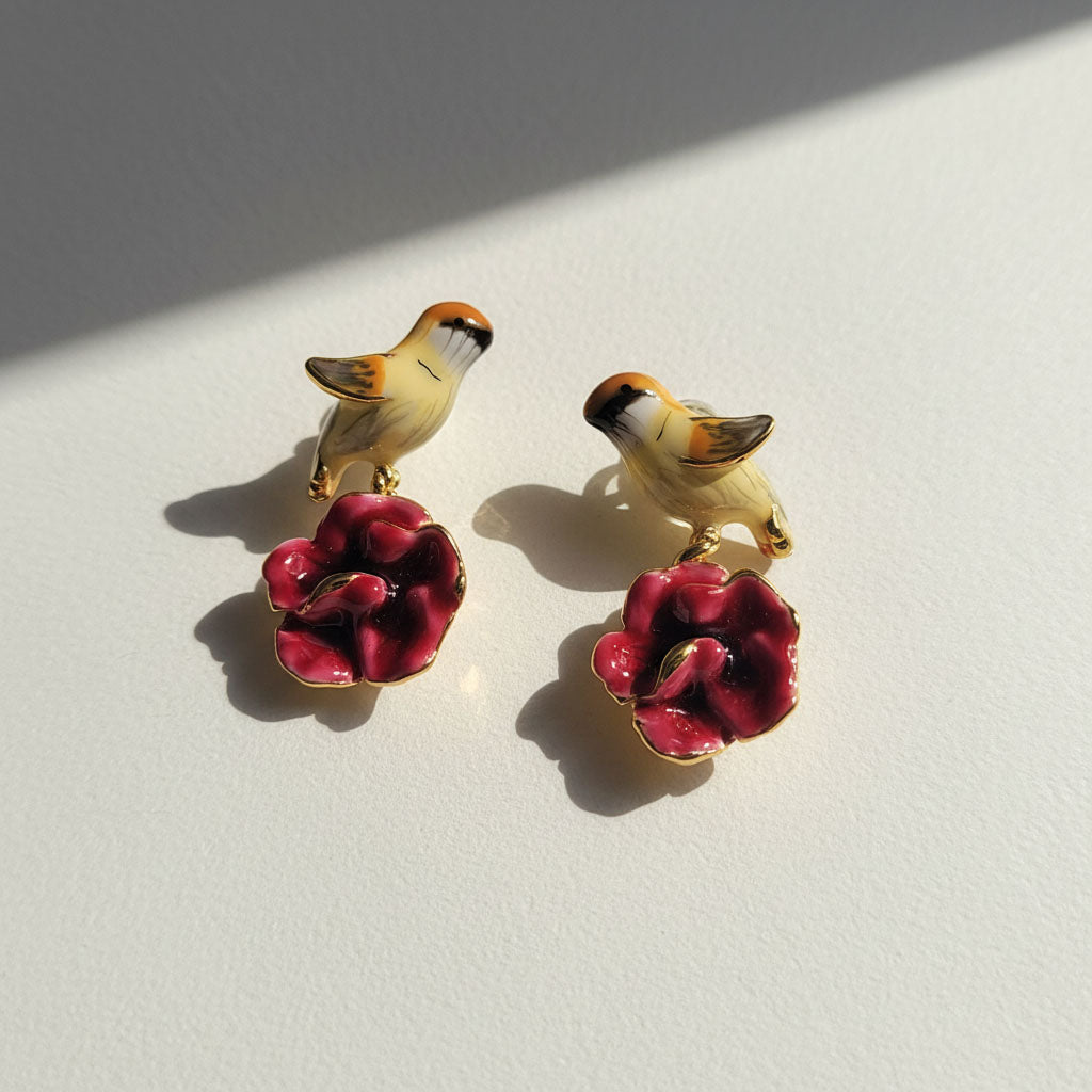 Pair of earrings with bird and flower design on a light background