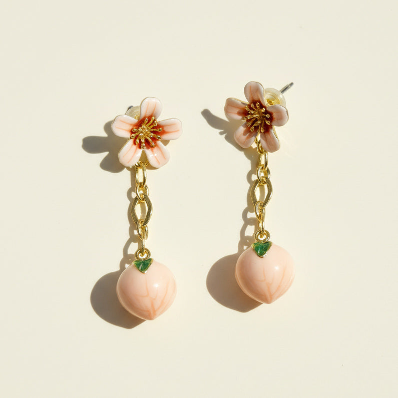 Pair of floral earrings with pink flowers and peach-like bottoms on a beige background