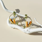 Earrings with animal designs on a branch against a beige background